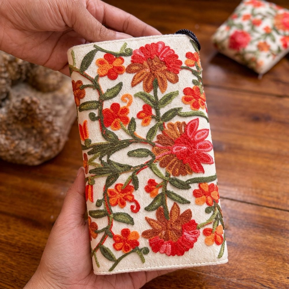 Handheld view of a cream wallet with red and orange floral embroidery
